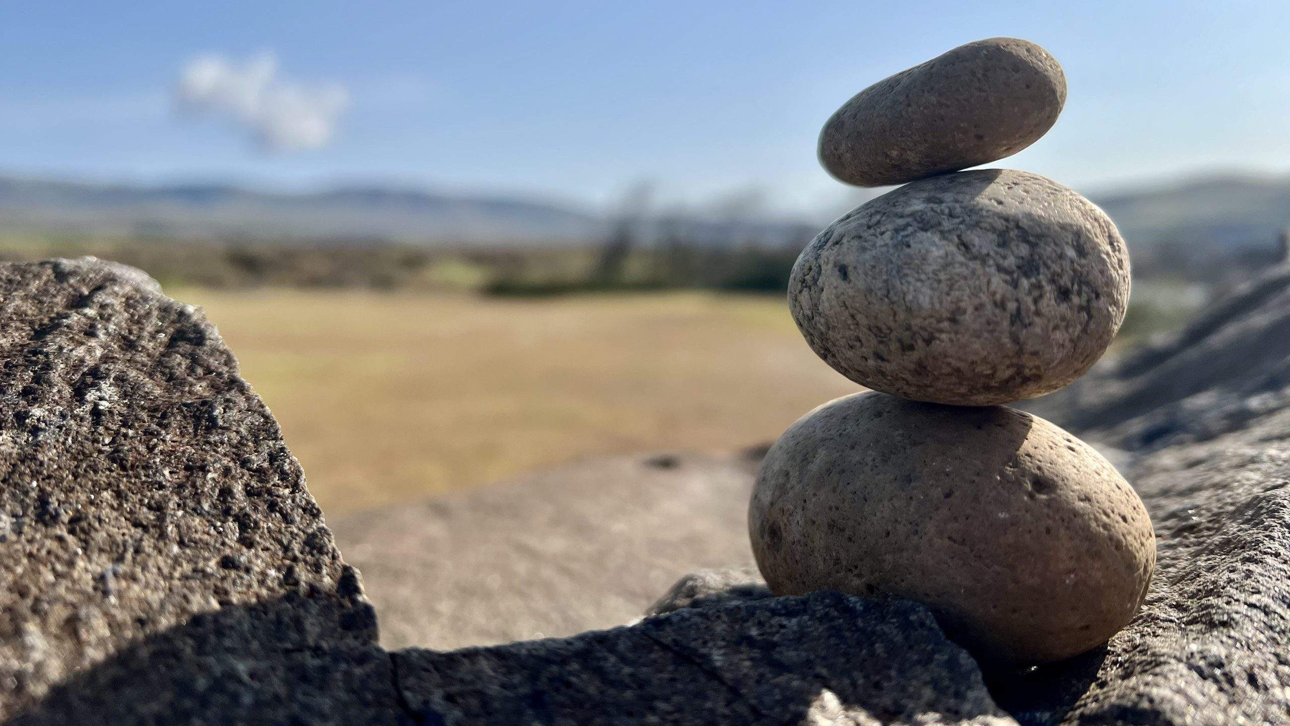 A stack of rocks balanced atop another rock with a dry landscape in the background.