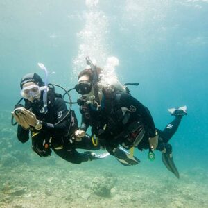 Two divers underwater using a compass for navigation.