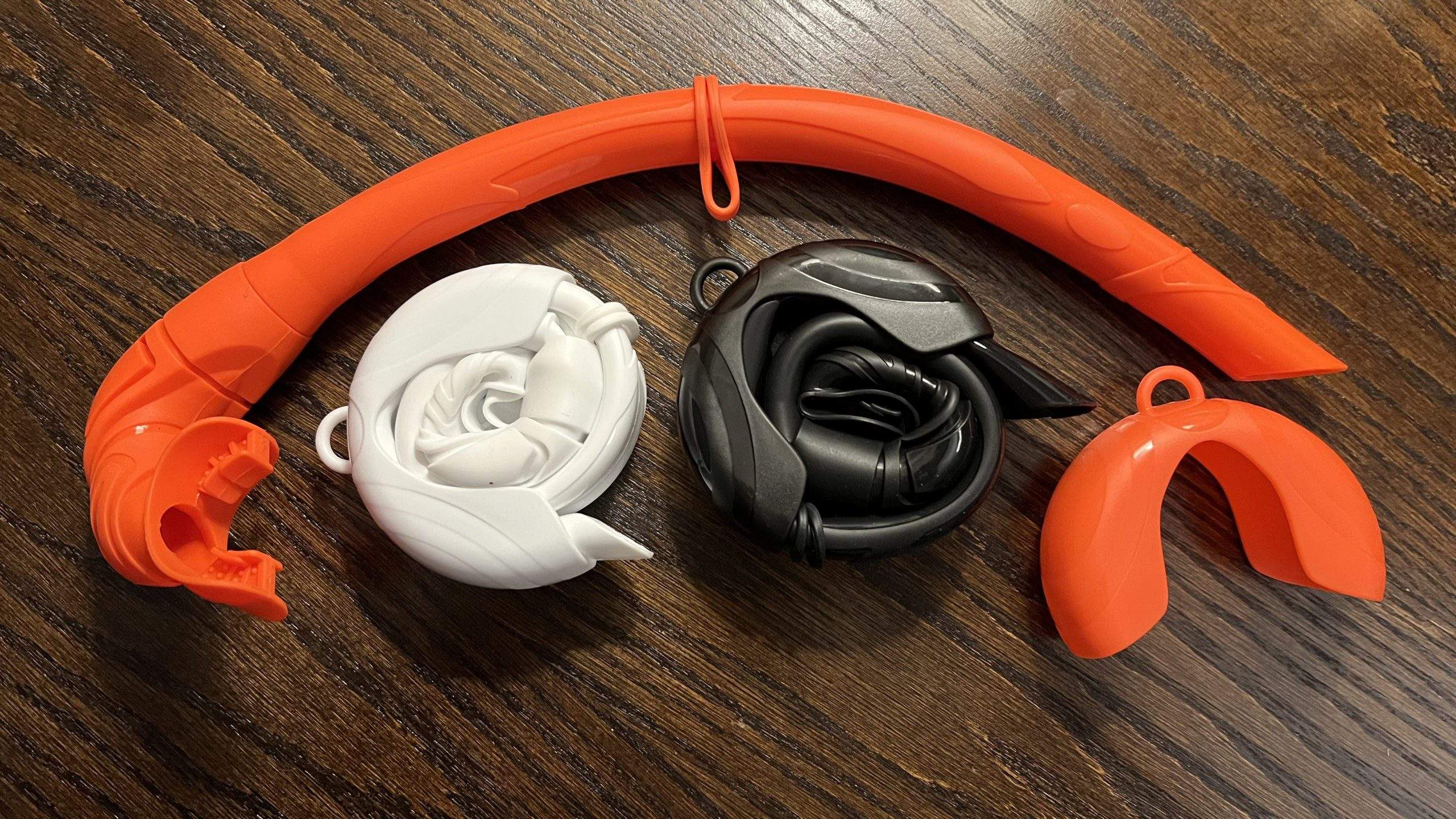 Three foldable silicone snorkels of different color: orange, black, and white.