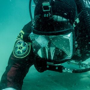 A public safety diver wearing a full face mask is searching with the left hand out diving through the created silt.