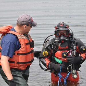 A public safety diver is egressing the water attached to a harness which is controlled by their tender.