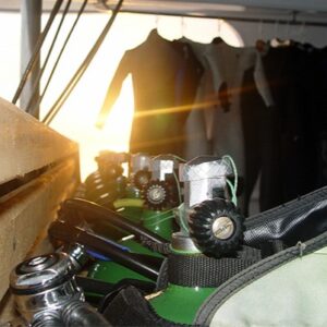 Sunlight streaming through wetsuits hanging to dry with cylinder valves glinting in the foreground.