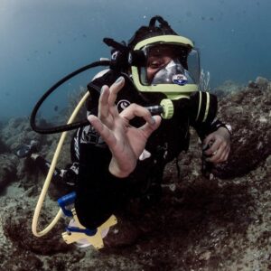 A SCUBA diver in full face mask sending the "OK" hand sign.