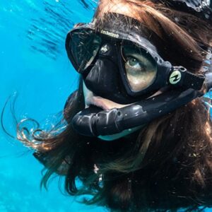 A young girl wearing a mask and snorkel in clear blue water.