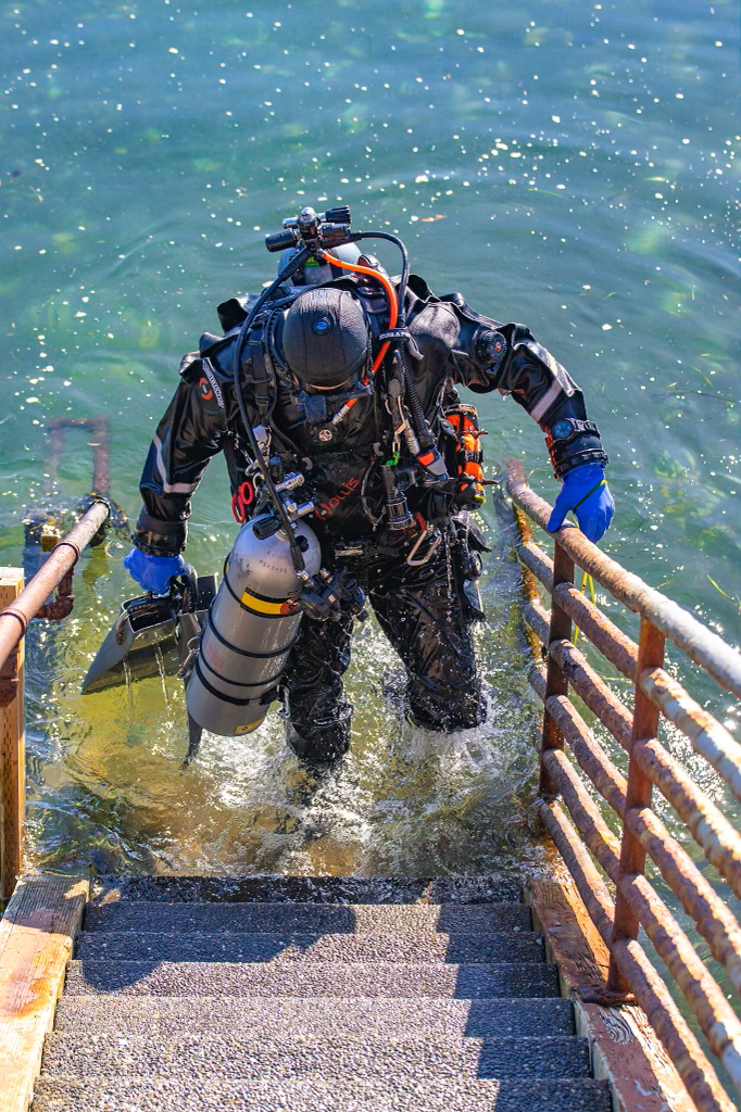 Image of a solo diver coming out of the water dressed in completely redundant gear.